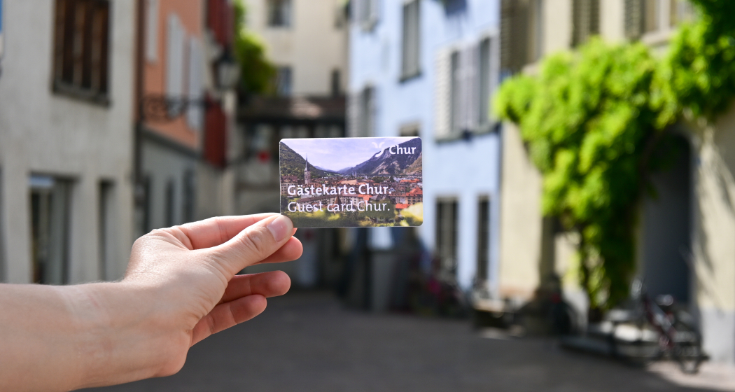 Gästekarte Chur Im Hintergrund sind Stadtmauern zu sehen, im Vordergrund hält eine Person die Gästekarte von Chur in den Händen.