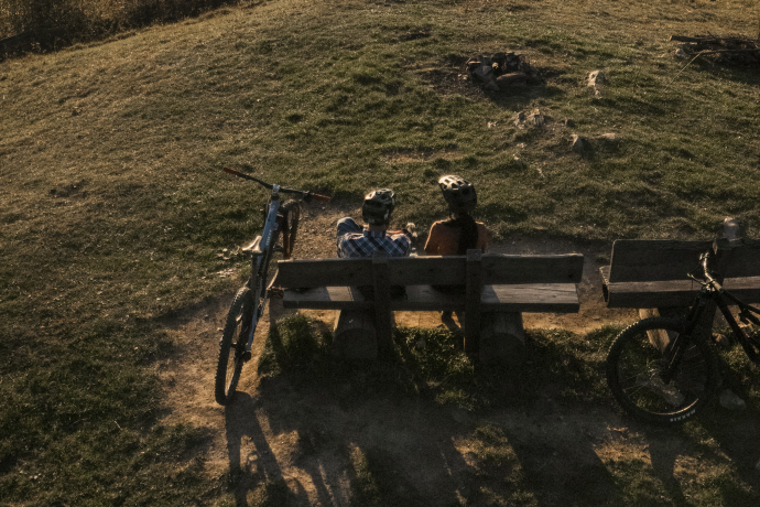 Bike auf dem Mittenberg (© Flavio Schlegel) Sonnenuntergang auf einem Berg mit Sicht auf die Stadt Chur, auf einem Bank sitzen zwei Personen