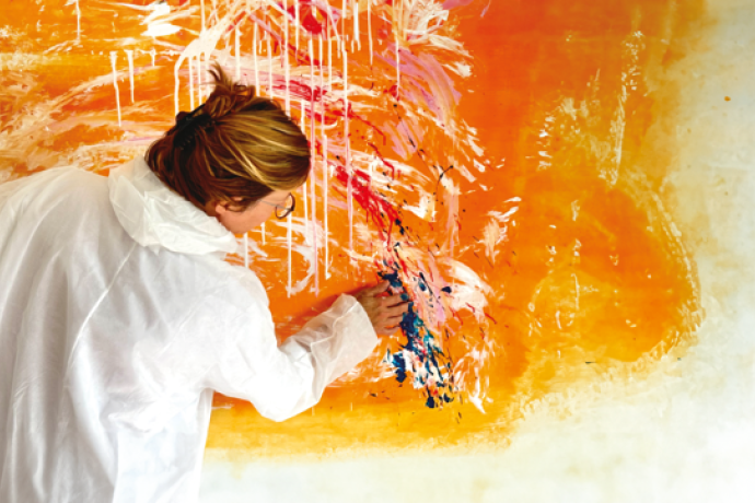 Mal Unquadrat (© Mal Unquadrat) A person in a white coat paints an abstract mural with bold orange and white strokes
