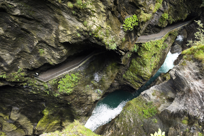 Viamala gorge (© Viamala tourism) A dramatic overhead view of a narrow mountain gorge with a winding walkway. Lush greenery clings to rocky walls above turquoise rapids below
