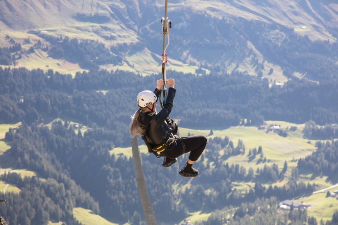 Zipline Pradaschier (© Pradaschier adventure mountain) A person zip lining above a lush, mountainous landscape. They wear a helmet and harness, conveying excitement and adventure