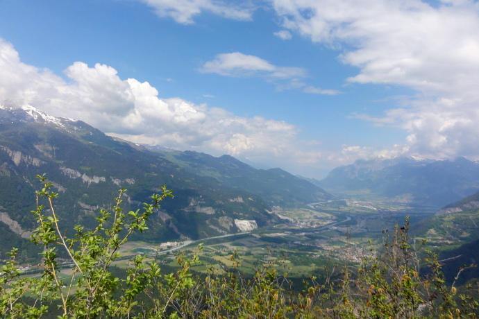 Rote Platte - Aussicht (© Michael Christ) Ein weiter Blick über das Churer Rheintal mit seinen grünen Feldern und der sich schlängelnden Rheinlinie. Umgeben von hohen Bergen mit teils schneebedeckten Gipfeln breitet sich die Landschaft unter einem leicht bewölkten Sommerhimmel aus.